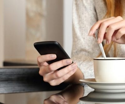 somebody looking at their phone whilst drinking a coffee