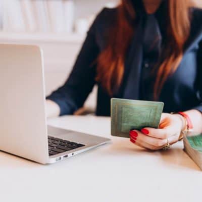 women with red hair holding a green tarot card in one hand with her laptop open