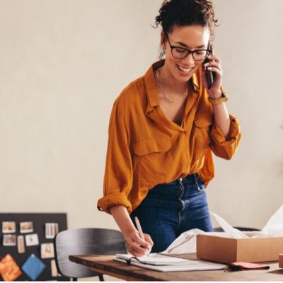 business womanstanding behind a text while speaking on the phone whilst writing notes on paper