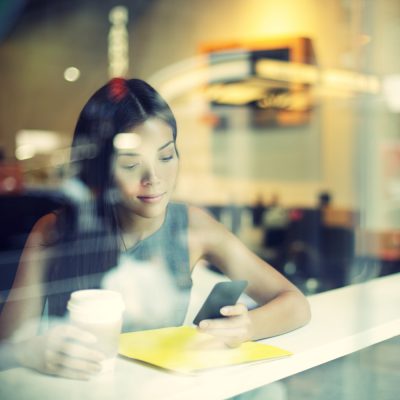 woman sitting at a high table with a coffee in one hand and her phone in her other hand